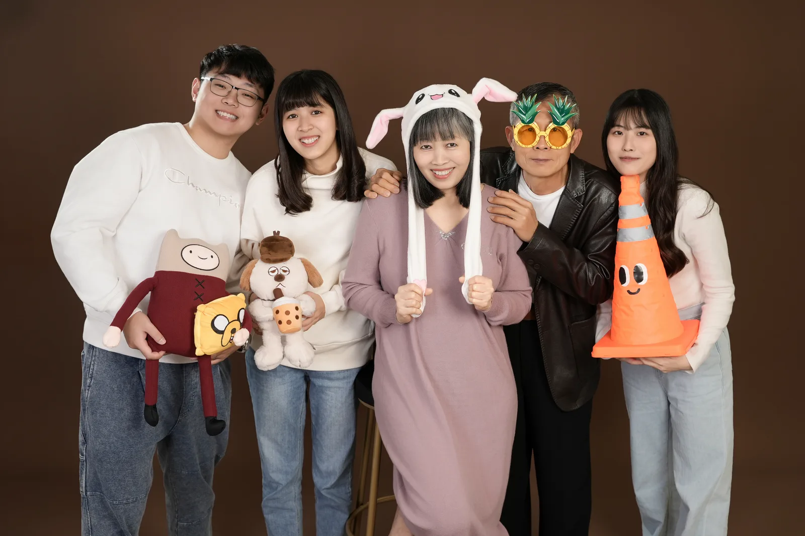 暖棕色背景五人全家福,家人拿著小道具,戴上不同造型配件