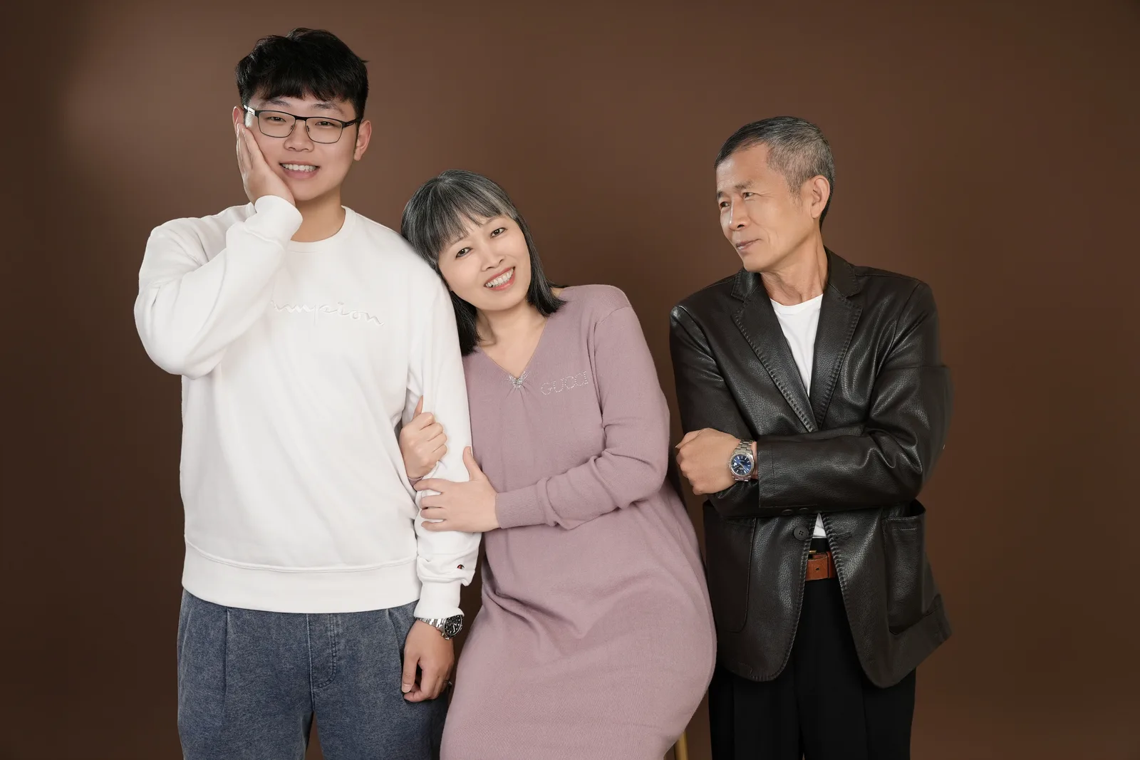 暖棕色背景三人小組合照,家人穿白色、淡紫色與深色外套並肩站著