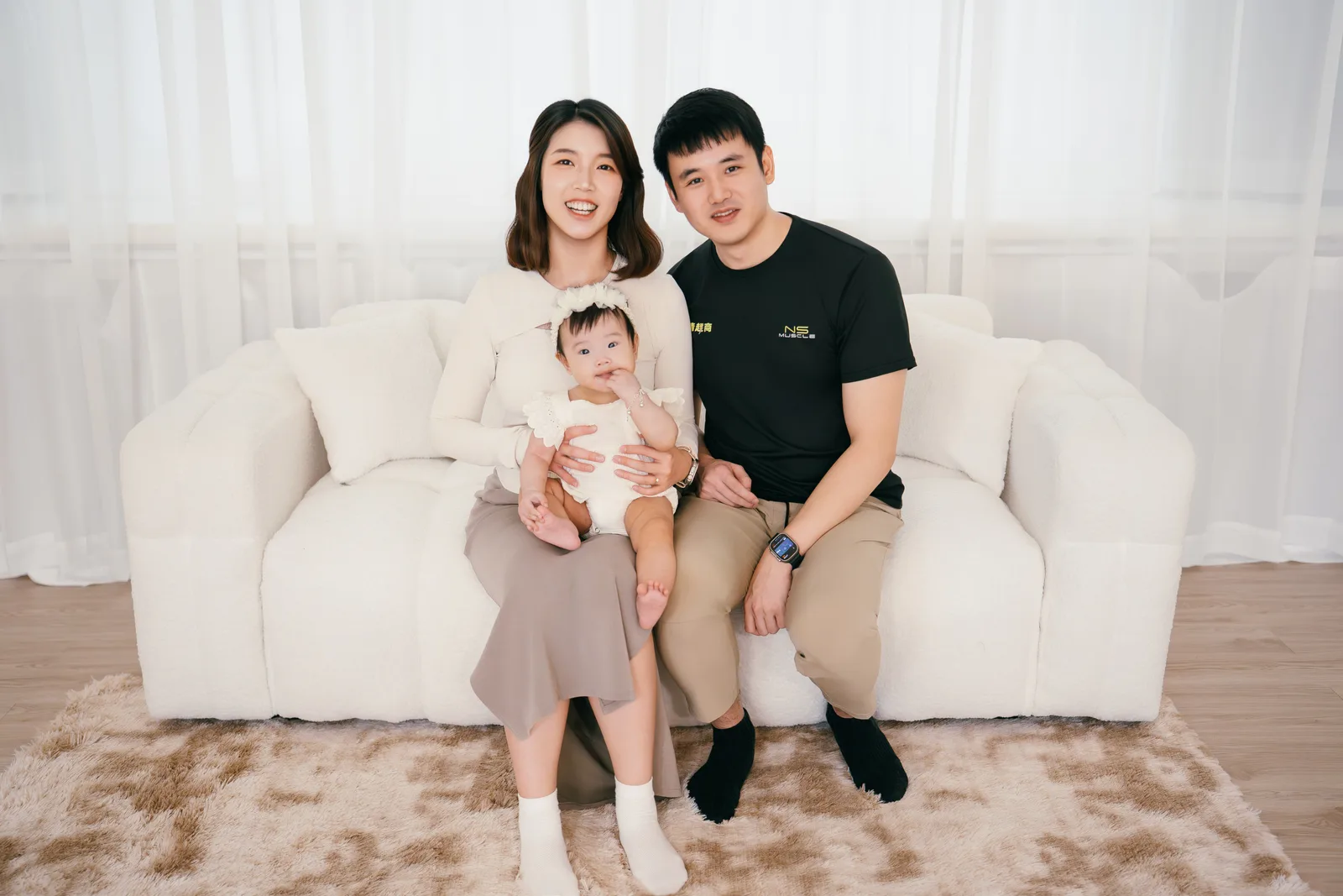 淺色棚景中的一家三口沙發合照,孩子坐在家人懷中
