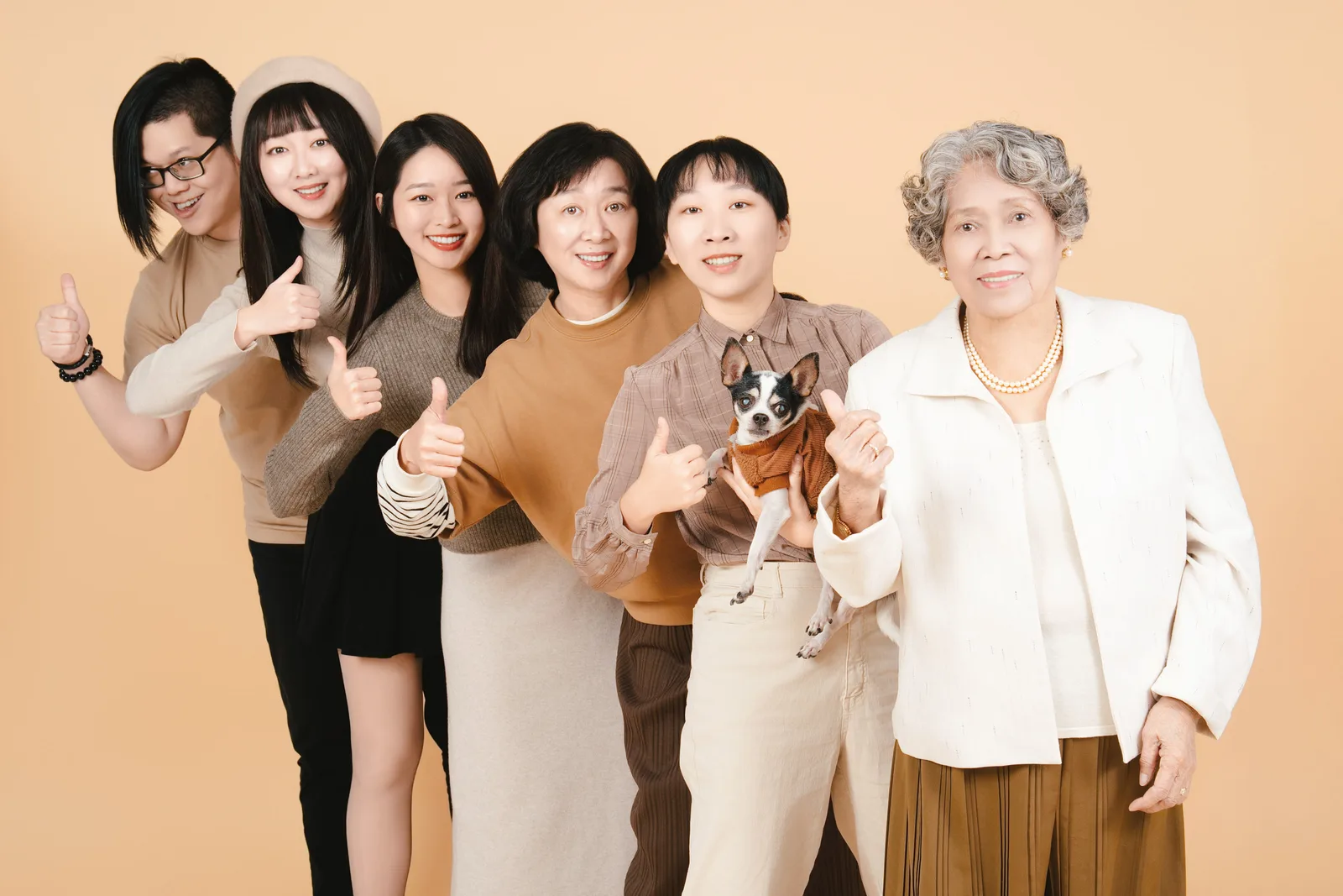 米色背景全家福,家人並肩微笑,前排家人抱著小狗